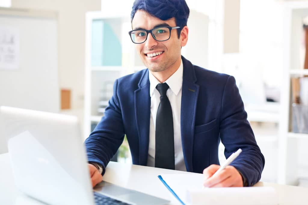 A professional man in glasses and a suit sits at a desk with a laptop, providing comprehensive service.
