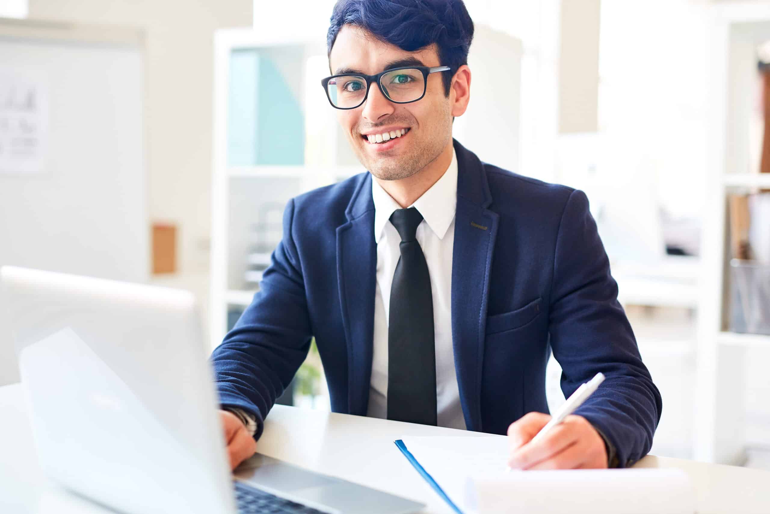 A professional man in glasses and a suit sits at a desk with a laptop, providing comprehensive service.